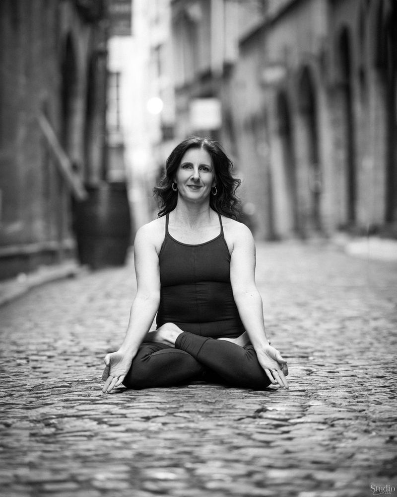 Valérie assise en lotus dans une rue pavée